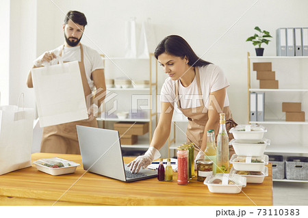 Meal delivery workers taking online orders and packing food in containers and paper bags 73110383