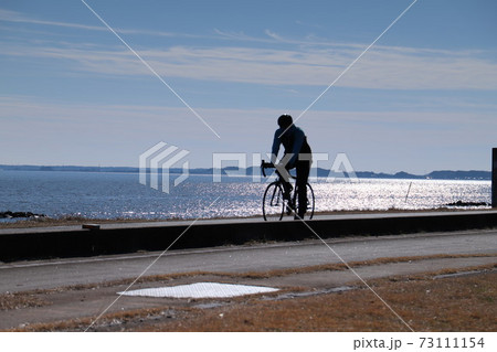 霞ヶ浦に反射する光を浴びながらつくば霞ヶ浦りんりんロードを走るサイクリスト 73111154