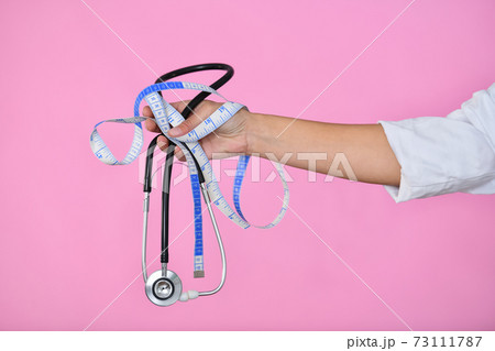 Doctor hand holding a measuring tape and a stethoscope Doctor hand holding a measuring tape and a stethoscope 73111787