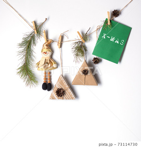 Decorative decoration for Christmas and New Year. Gifts, a toy snowman, pine branches, cones are attached to the rope with clothespins. Eco-friendly holiday concept. White background and place for an 73114730