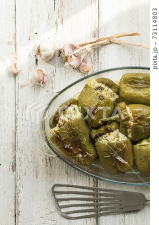 Pepper stuffed with white cheese, herbs, garlic. Glass dish prepared with seasonal local vegetables. White wood background. Soft focus 73114803