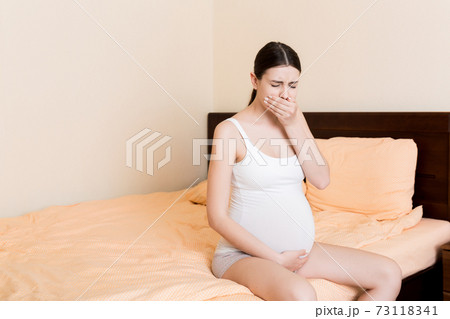 Pregnant suffering with nausea. Pregnancy symptoms, expectation toxicosis. Young vomiting woman sitting on bed. parenthood concept Pregnant suffering with nausea. Pregnancy symptoms, expectation toxicosis. Young vomiting woman sitting on bed. parenthood concept 73118341