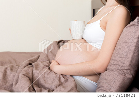 pregnant young woman sitting on bed and drinking coffee at home. maternity concept 73118421