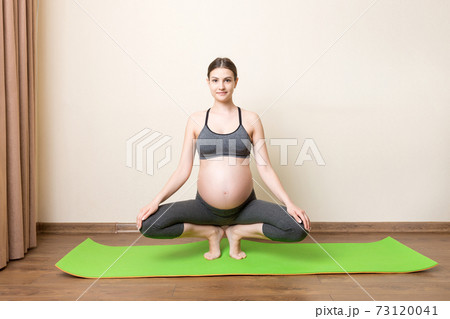 beautiful young pregnant woman sitting on mat in yoga pose at the home. Pregnancy Yoga and Fitness concept at coronavirus time 73120041