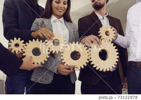 Smiling young business people colleagues or team fixing wooden gears together 73122978