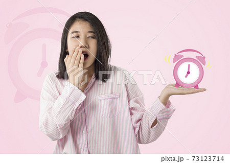 woman wear pink pajamas yawn and holding alarm clock  feeling sleepy 73123714