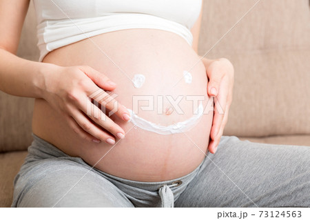 a pregnant girl sits at home on the bed and smears smile an anti-stretch mark cream on her stomach. Pregnancy, motherhood, preparation and expectation concept a pregnant girl sits at home on the bed and smears smile an anti-stretch mark cream on her stomach. Pregnancy, motherhood, preparation and expectation concept 73124563