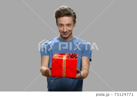 Handsome teen boy offering gift box to someone. 73124771