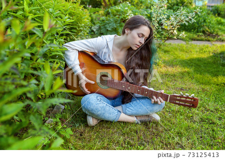 Young woman sitting in grass and playing guitar 73125413