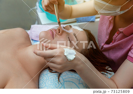 Woman getting face treatment with white nourishing creme in spa salon Woman getting face treatment with white nourishing creme in spa salon 73125809