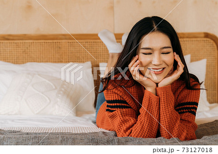 Young teenage Asian woman wears a sweater with pretty smile looking at camera in bedroom. Attractive girl with facial treatment and healthy beauty skin Winter portrait fashion lifestyle. Banner space. 73127018
