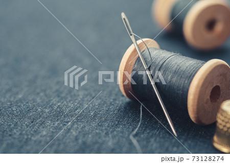 Wooden spools of blue thread and thimble on blue jeans cloth. 73128274