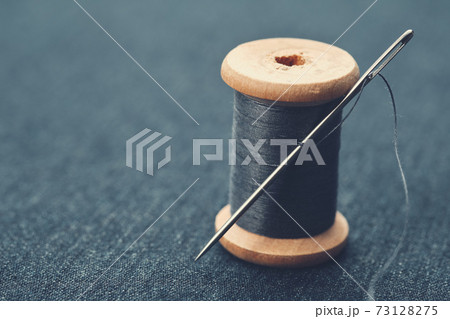 Wooden spool of blue thread on blue jeans cloth. Needle and thread through. 73128275
