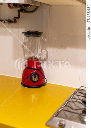 Red electronic mixer stands on a yellow table near the stove in the kitchen Red electronic mixer stands on a yellow table near the stove in the kitchen 73128484