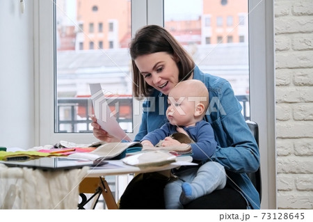 Young mother work with baby in her arms at home office Young mother work with baby in her arms at home office 73128645