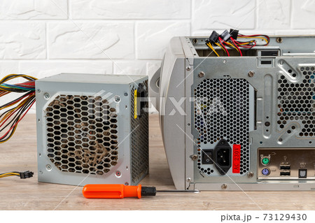 Old faulty power supply unit and a screwdriver near tower case with installed new one on a desk. Old faulty power supply unit and a screwdriver near tower case with installed new one on a desk. 73129430