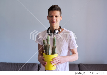 Portrait of teenage boy in headphones holding pot of cacti in his hands Portrait of teenage boy in headphones holding pot of cacti in his hands 73132862