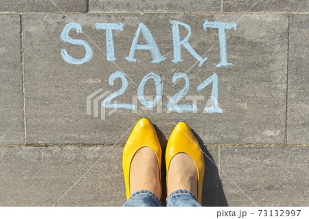Start 2021 year concept, top view on woman legs and text written in chalk on gray sidewalk 73132997