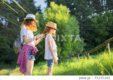 Summer, happy kids walking enjoying nature vacation, older sister braids her younger hair Summer, happy kids walking enjoying nature vacation, older sister braids her younger hair 73135282