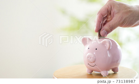 豚の貯金箱に硬貨を入れる男性 73138987