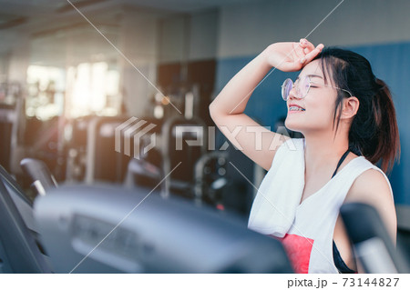 Asian teenage braces girl cardio training exercise in sport club with towel on her shoulders smiling after workout on treadmill in the gym looking camera. 73144827