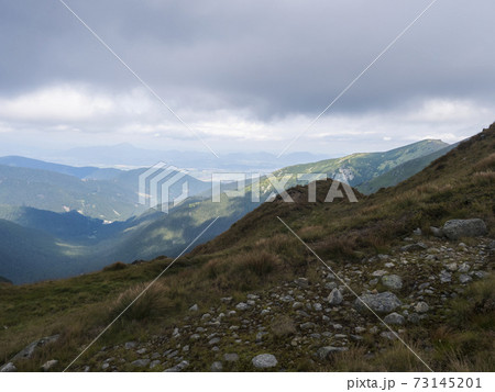 View from grassy hill slopes of hiking trail from Chopok at mountain meadow ridge Low Tatras mountains, Slovakia. Fog and clouds, late summer day 73145201