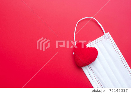 heart shape decoration and Medical face mask on red background against Coronavirus disease infection. Love, together and Happy Valentines day under Covid-19 pandemic concept heart shape decoration and Medical face mask on red background against Coronavirus disease infection. Love, together and Happy Valentines day under Covid-19 pandemic concept 73145357