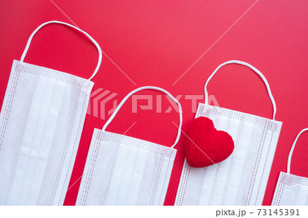 heart shape decoration and Medical face mask on red background against Coronavirus disease infection. Love, together and Happy Valentines day under Covid-19 pandemic concept 73145391