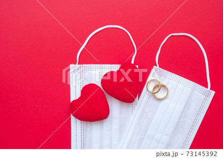 heart shape decoration, golden engagement ring and Medical face mask on red background against Coronavirus disease infection. Love, together and Happy Valentines day under Covid-19 pandemic concept heart shape decoration, golden engagement ring and Medical face mask on red background against Coronavirus disease infection. Love, together and Happy Valentines day under Covid-19 pandemic concept 73145392