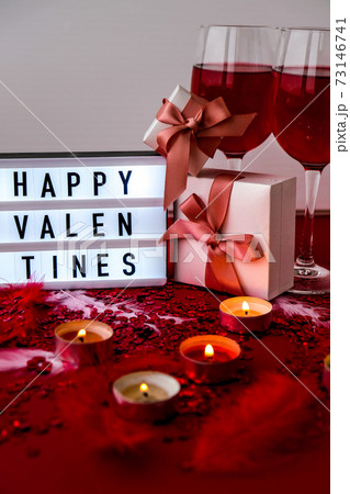 Lightbox with text HAPPY VALENTINES two glasses of red wine and gift boxes Burning red candles on confetti sequinned background with feathers. Saint Valentines Day and Christmas background . Lightbox with text HAPPY VALENTINES two glasses of red wine and gift boxes Burning red candles on confetti sequinned background with feathers. Saint Valentines Day and Christmas background . 73146741
