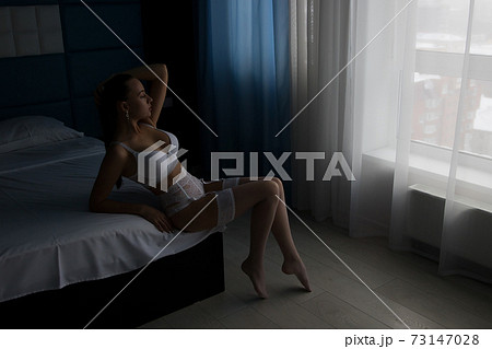 Seductive woman in lingerie sitting on bed 73147028