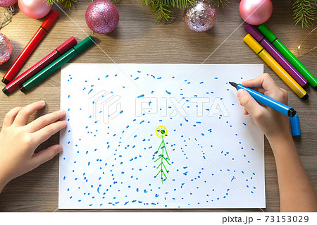 The child's hands draw a Christmas tree with markers on paper 73153029
