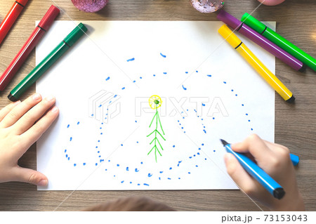 The child's hands draw a Christmas tree with markers on paper 73153043