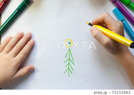 The child's hands draw a Christmas tree with markers on paper 73153062
