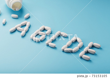 Pour the letter of vitamin A B C D E in capsules from a jar on a blue background 73153105