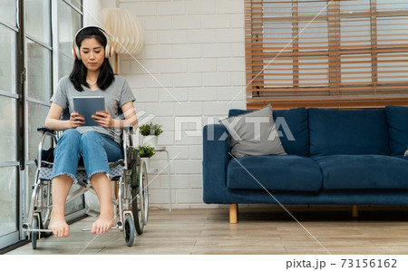 Happy disabled Asian woman sitting in a wheelchair And working with tablet at home, The concept of Technologies for the convenience of people with disabilities. Happy disabled Asian woman sitting in a wheelchair And working with tablet at home, The concept of Technologies for the convenience of people with disabilities. 73156162