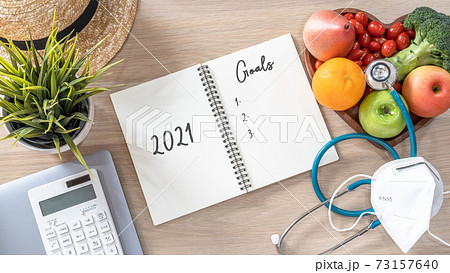 2021 goals on note book for new year list reminder in notebook of yearly planner and health plan for work-life balance on desk background of computer, healthy food, face mask for covid-19 protection 73157640