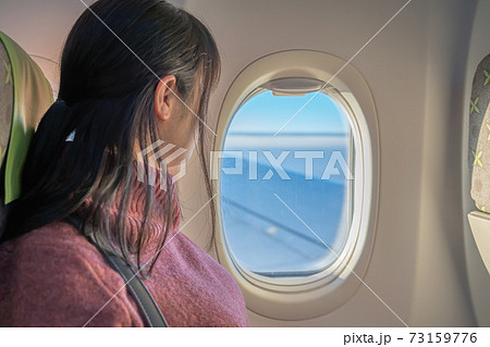 飛行機の中から窓の外を眺める赤い服の美しい女性 73159776