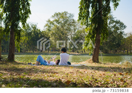 asian couple picnic with happiness feeling in park with lake in springtime 73159838