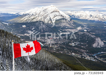 Close-up National Flag of Canada with Town of Banff, Cascade Mountain and surrounding snow-covered Canadian Rocky Mountains in winter. Banff National Park, Alberta, Canada. 73160949