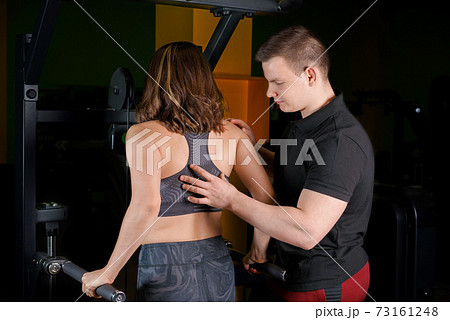 The trainer helps the girl do the triceps exercise. The trainer helps the girl do the triceps exercise. 73161248