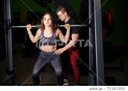 The trainer helps the girl to perform the exercise on the Schmitt simulator. 73161303