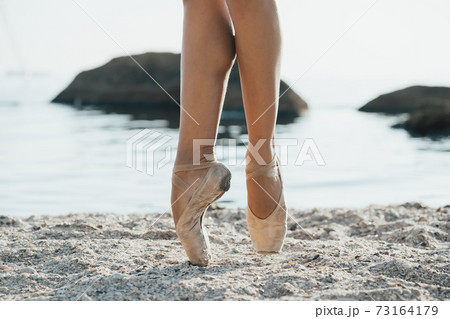 Close up of ballet dancer's feet. She practices exercises on sandy beach. Woman's legs in pointe Close up of ballet dancer's feet. She practices exercises on sandy beach. Woman's legs in pointe 73164179