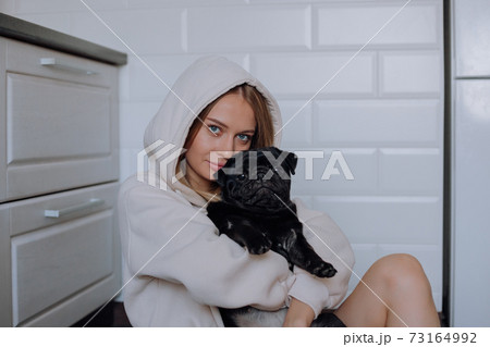 Girl holds a black pug dog in her arms at home Girl holds a black pug dog in her arms at home 73164992