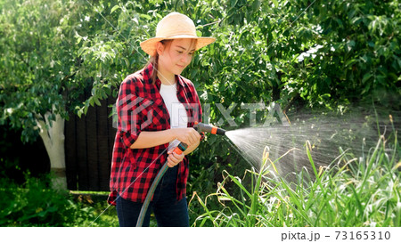 Young woman in farmer hat watering green organic vegetables growing at orchard. People working at backyard garden and orchard 73165310