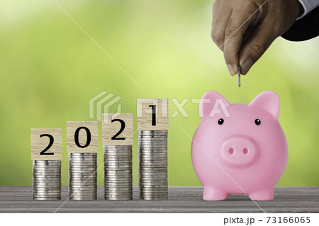 Businessman hand putting coin into piggy bank with saving growth year 2021 on stacking coin growing, meaning of earning money or investment or financial or tax for business advertising concept 73166065