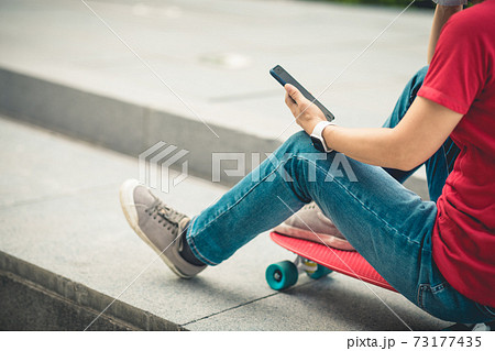 Asian woman sit on skateboard using smartphone in modern city 73177435