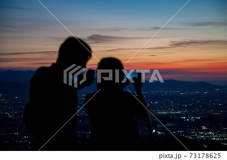夕景の写真を撮るカップルの後ろ姿の写真素材