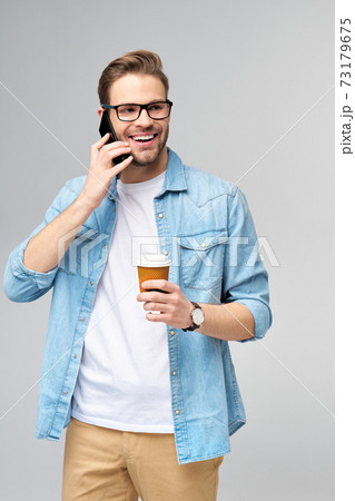 pretty casual man in blue jeans shirt holding his phone and cup of coffee to go standing over studio grey background pretty casual man in blue jeans shirt holding his phone and cup of coffee to go standing over studio grey background 73179675