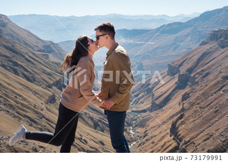 Brunette with long hair holds guy hands against canyon Brunette with long hair holds guy hands against canyon 73179991